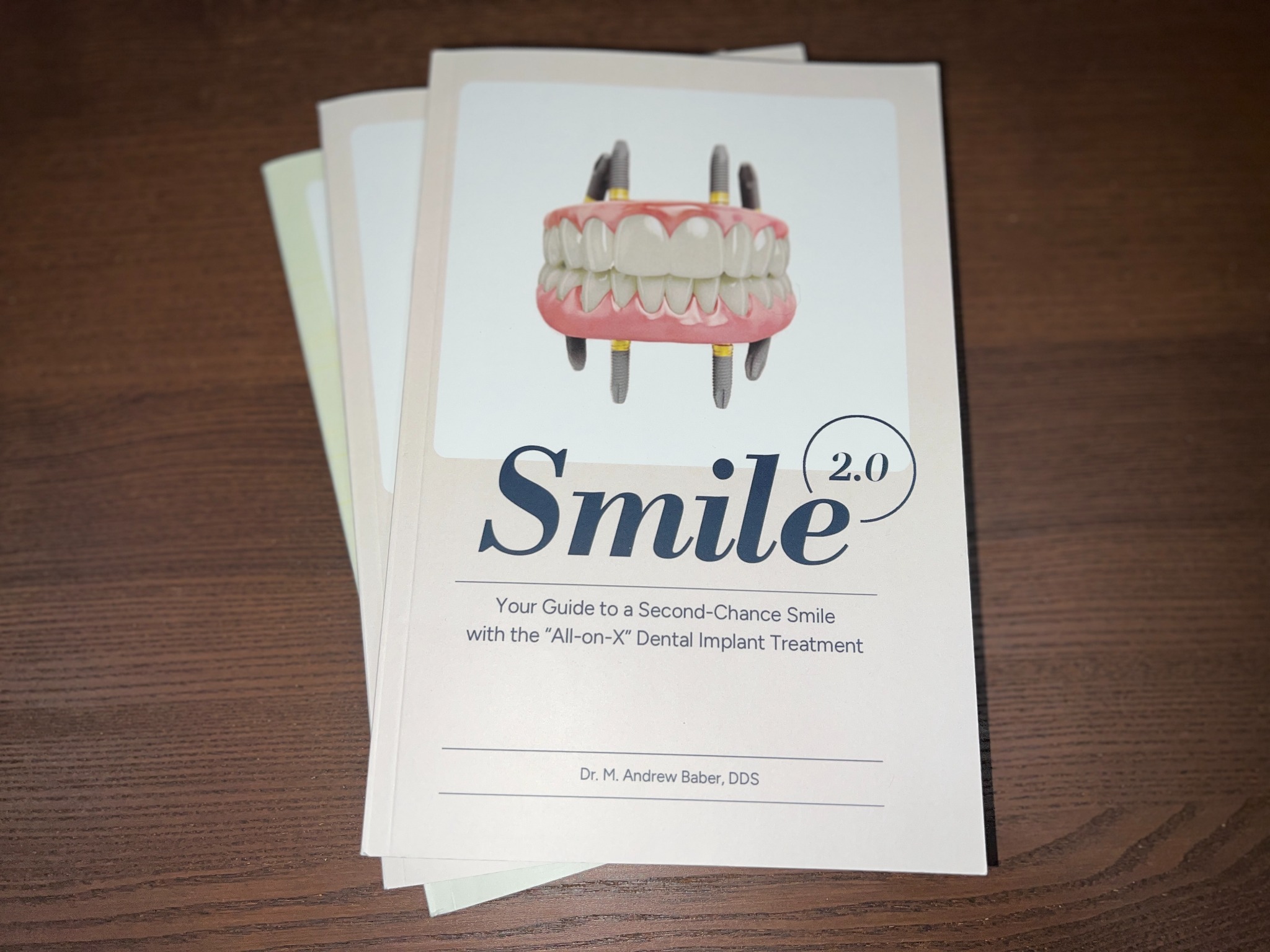 Printed copies of Smile 2.0 by Dr. M. Andrew Baber on a wooden table.